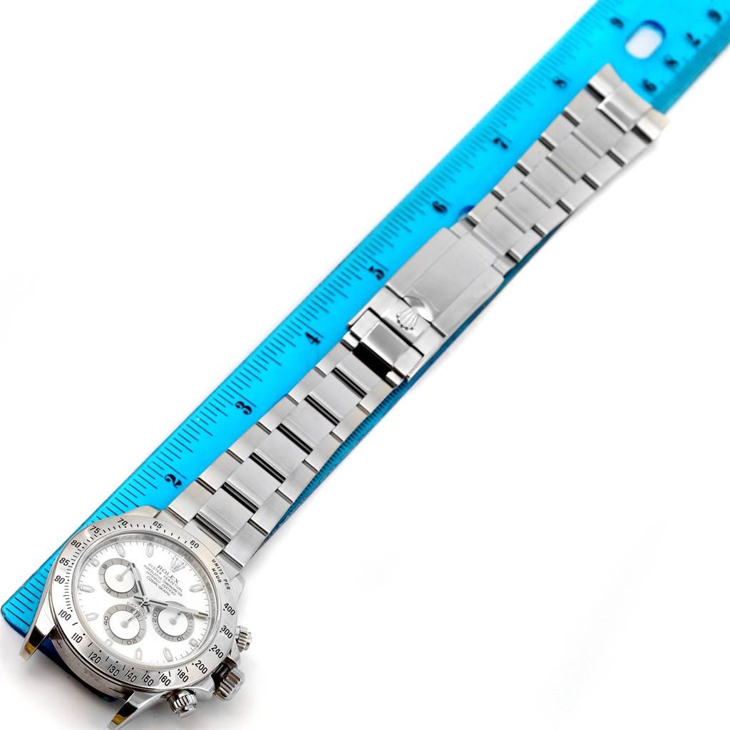 The image shows the Rolex Daytona 116520 Men's Stainless Steel White Dial 116520 Men's Stainless Steel White Dial watch lying flat with a metal bracelet and clasp next to a blue ruler.