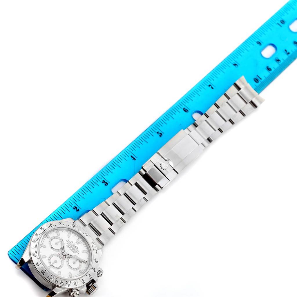 The image shows a Rolex Daytona 116520 Men
s Stainless Steel White Dial 116520 Men
s Stainless Steel White Dial watch laid flat next to a blue ruler, highlighting its bracelet and face.