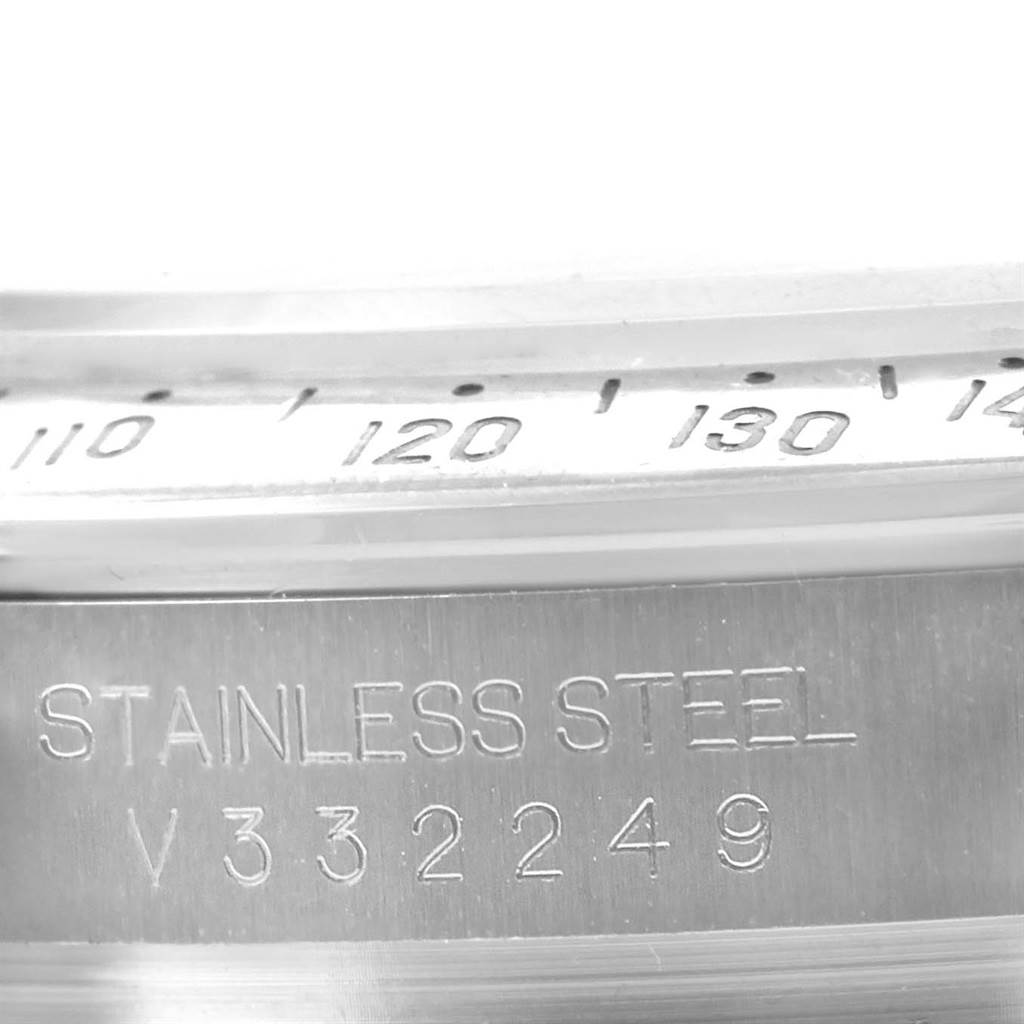 The image shows a close-up of the Rolex Daytona 116520 Men's Stainless Steel White Dial 116520 Men's Stainless Steel White Dial's bezel and engraved case back with the serial number and "STAINLESS STEEL."