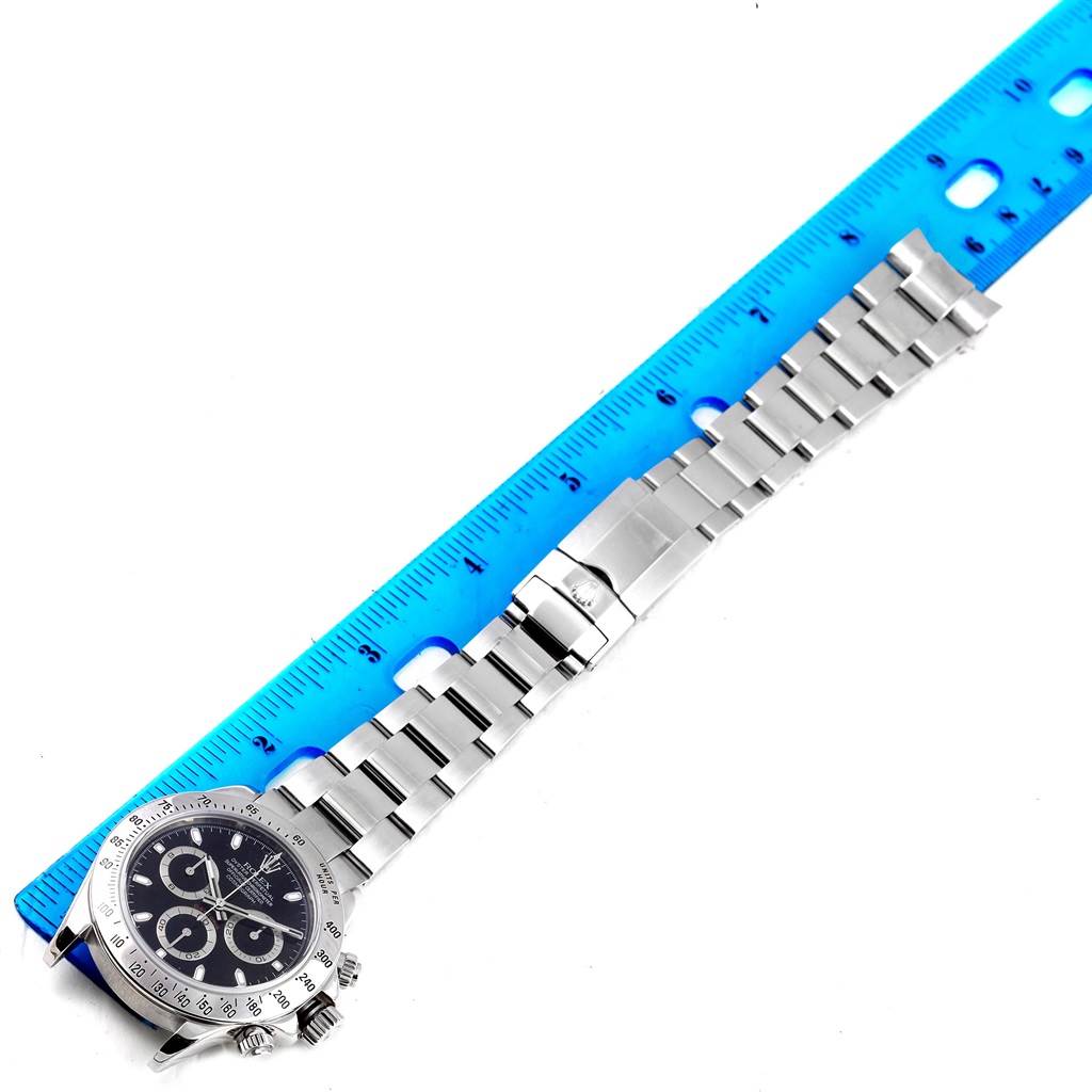 The image shows a top-down view of a Rolex Daytona 116520 Men's Stainless Steel Black Dial 116520 Men's Stainless Steel Black Dial watch with its stainless steel bracelet next to a blue ruler.