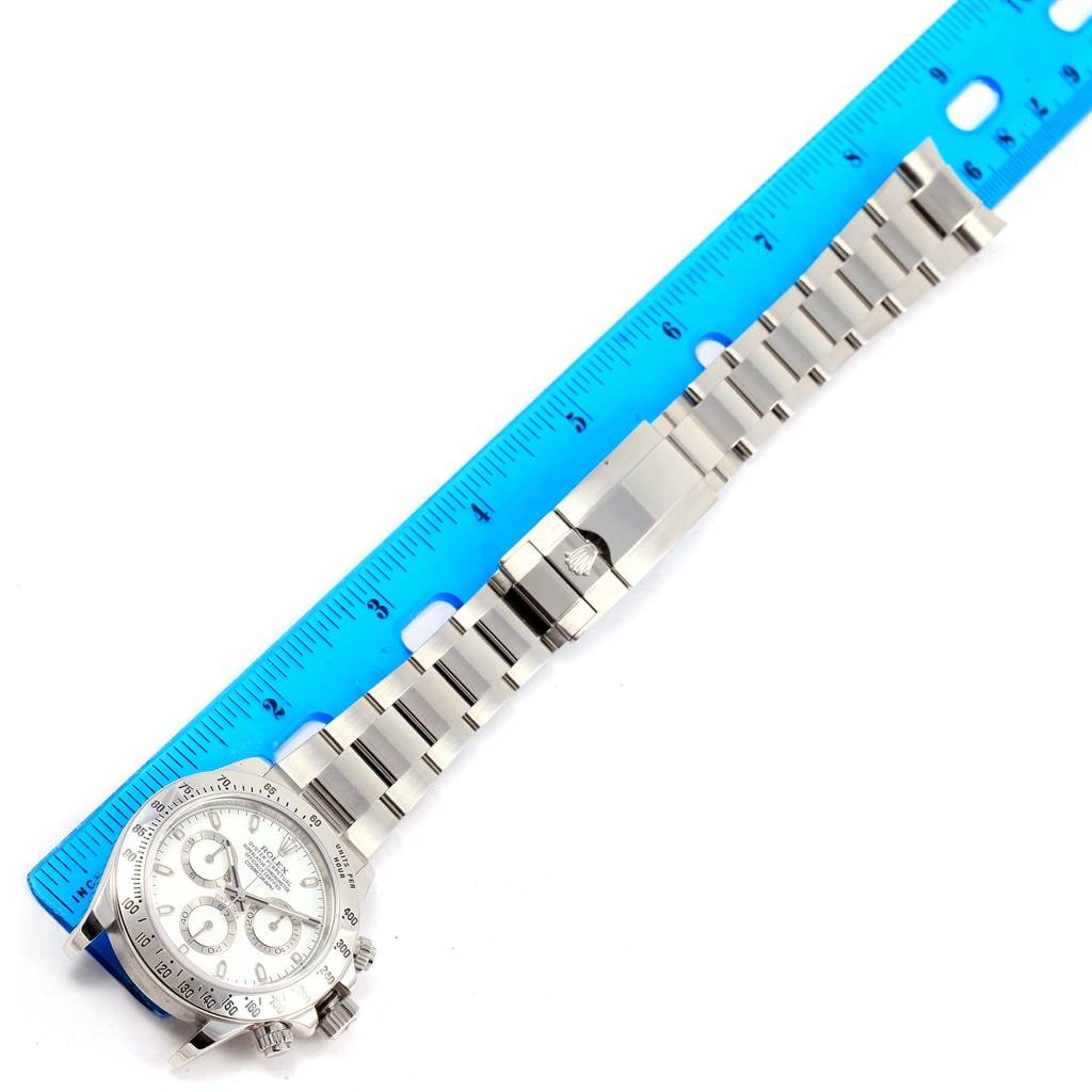 The image displays a Rolex Daytona 116520 Men's Stainless Steel White Dial 116520 Men's Stainless Steel White Dial watch laid flat with its full bracelet and a clasp, next to a blue ruler for scale.