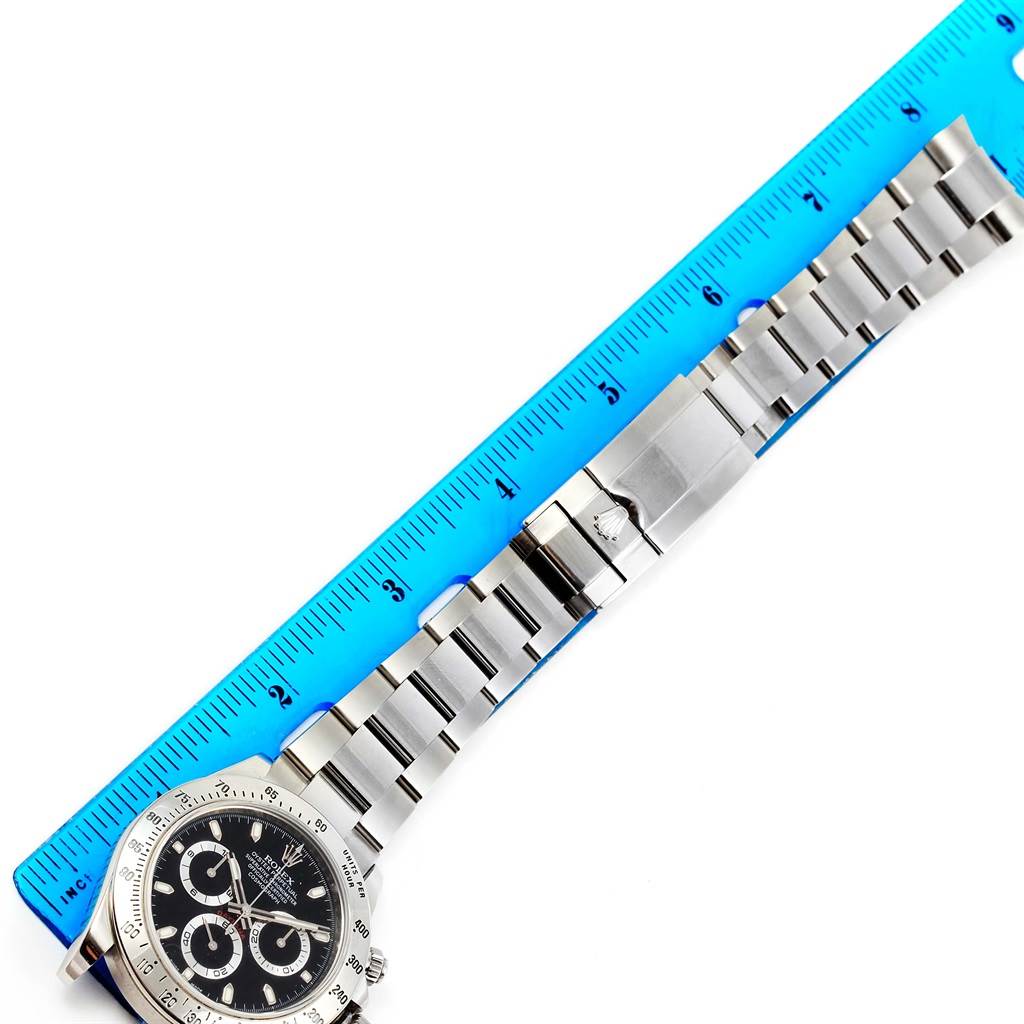 This image shows a Rolex Daytona 116520 Men's Stainless Steel Black Dial 116520 Men's Stainless Steel Black Dial watch placed next to a blue ruler, highlighting the watch band and clasp.