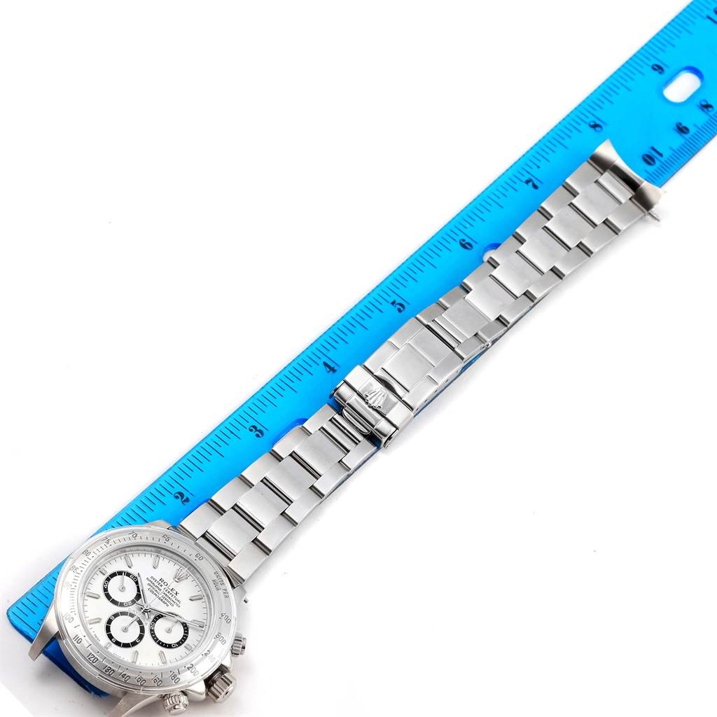 The image shows a Rolex Daytona 16520 Men
s Stainless Steel White Dial 16520 Men
s Stainless Steel White Dial watch laid flat next to a ruler, displaying its bracelet and a portion of the dial.