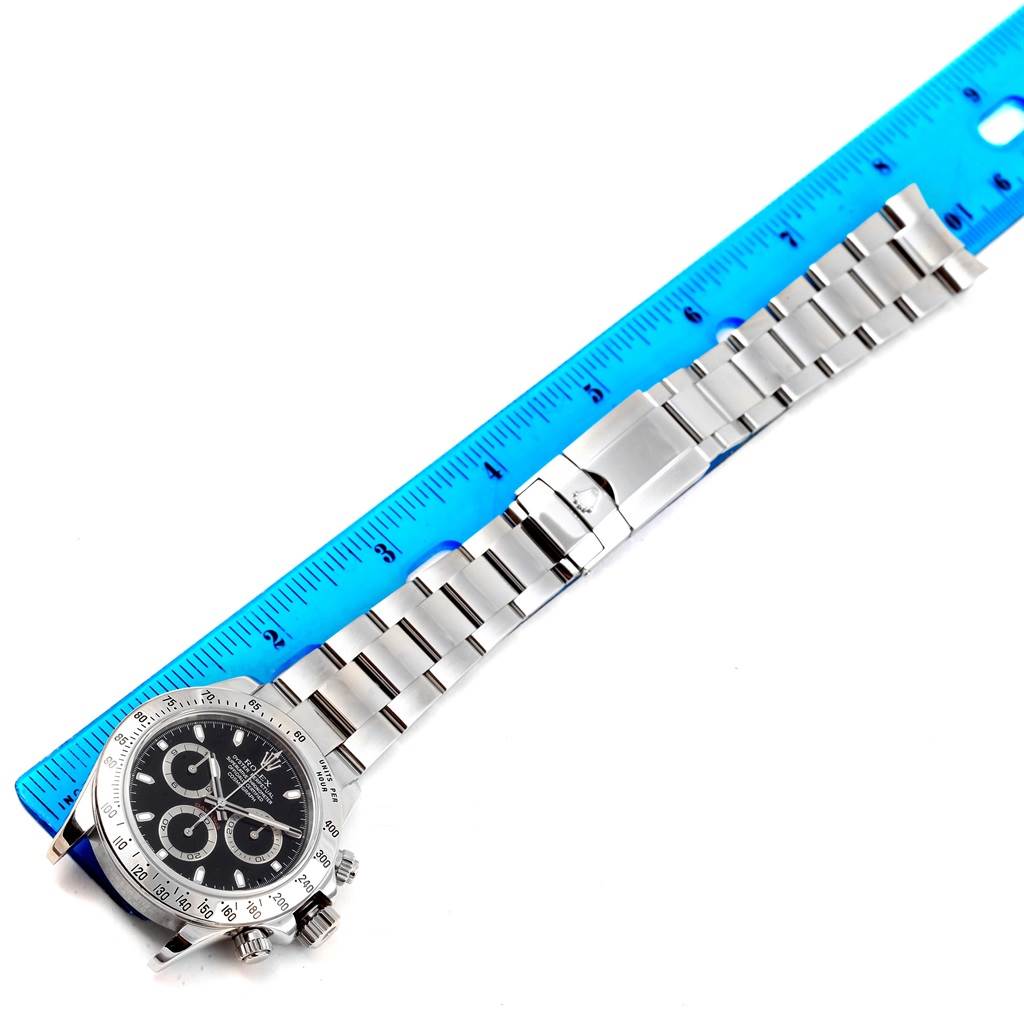 This image shows the Rolex Daytona 116520 Men's Stainless Steel Black Dial 116520 Men's Stainless Steel Black Dial watch laid flat, with its face and full bracelet visible next to a blue ruler.