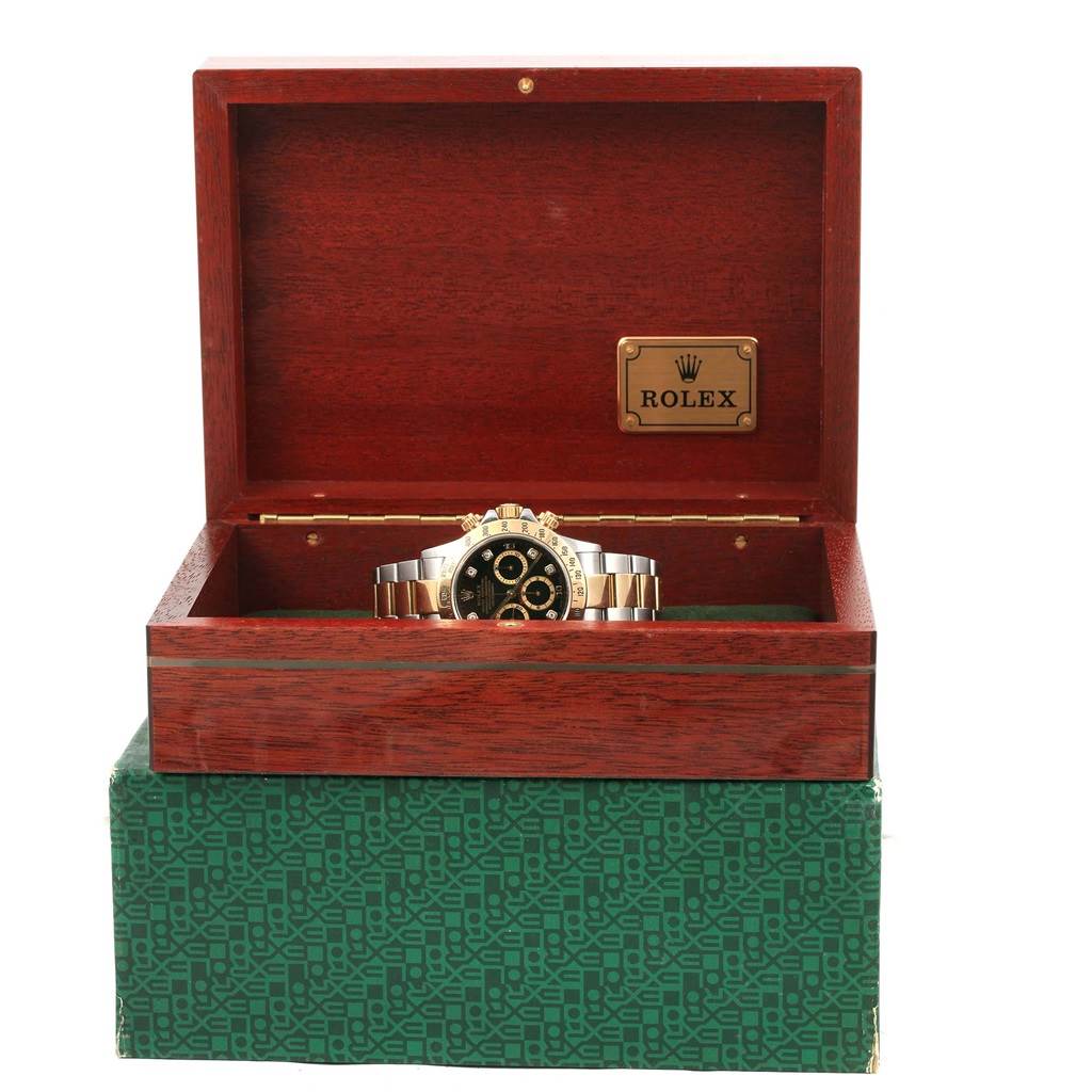 The Rolex Daytona 16523 Men's Steel and Gold (two tone) Black Dial 16523 Men's Steel and Gold (two tone) Black Dial watch is shown from a front angle, sitting inside an open Rolex wooden box on a green patterned box.