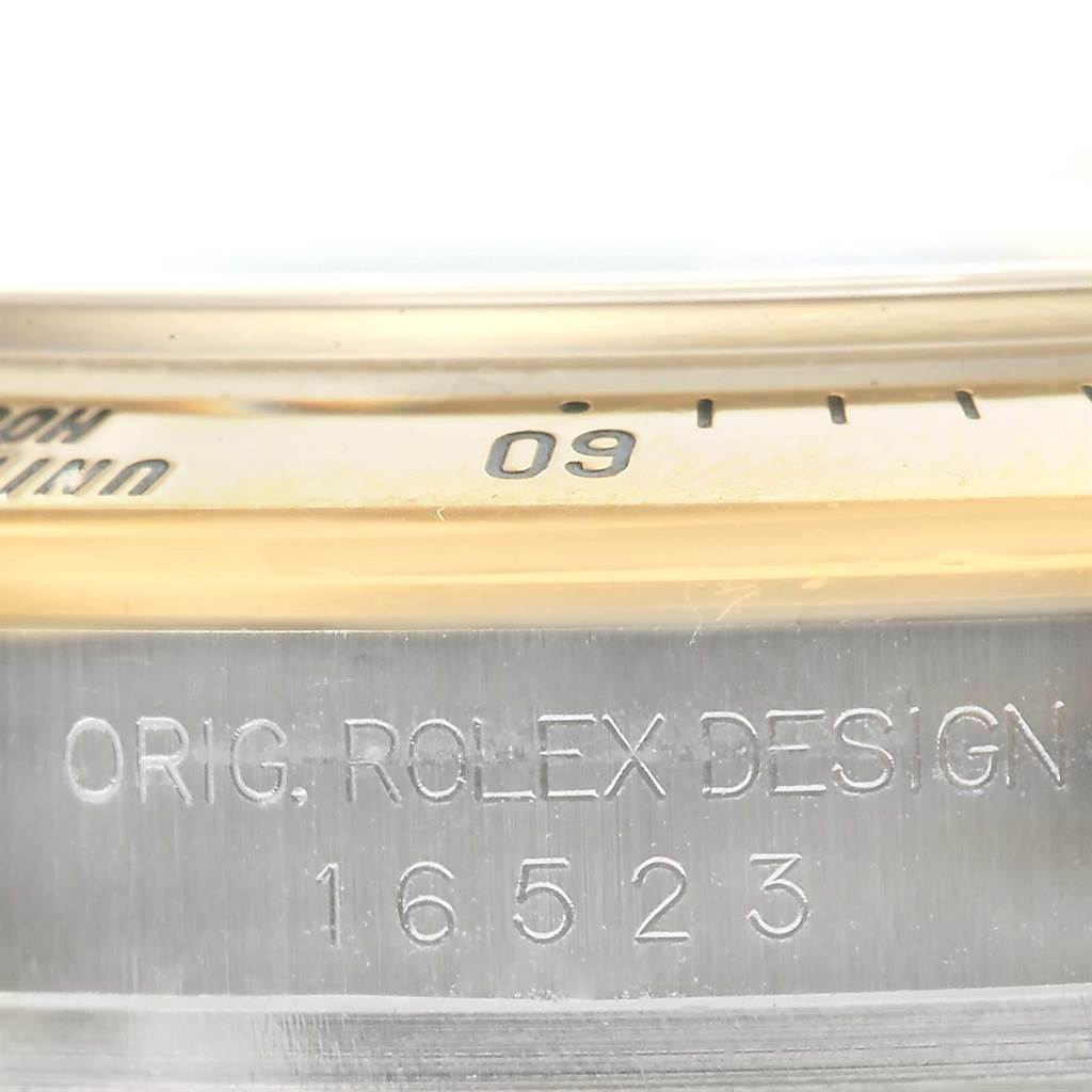 The image shows a close-up of the side engraving and a portion of the bezel of a Rolex Daytona 16523 Men's Steel and Gold (two tone) Black Dial 16523 Men's Steel and Gold (two tone) Black Dial watch.