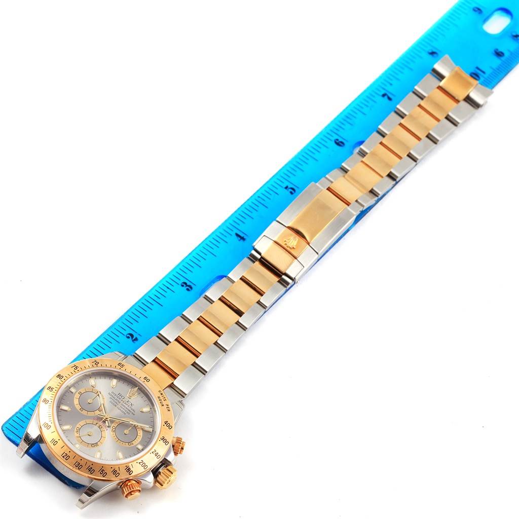 The image shows a Rolex Daytona 116523 Men's Steel and Gold (two tone) Grey Dial 116523 Men's Steel and Gold (two tone) Grey Dial watch laid flat with a ruler beside it, displaying the dial, bezel, and bracelet.