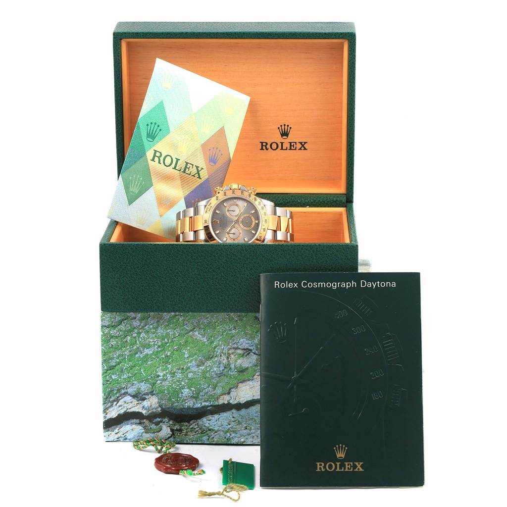 The image shows a Rolex Daytona 116523 Men's Steel and Gold (two tone) Grey Dial 116523 Men's Steel and Gold (two tone) Grey Dial watch inside its box, along with manuals and tags, with an angled front view of the box and accessories.
