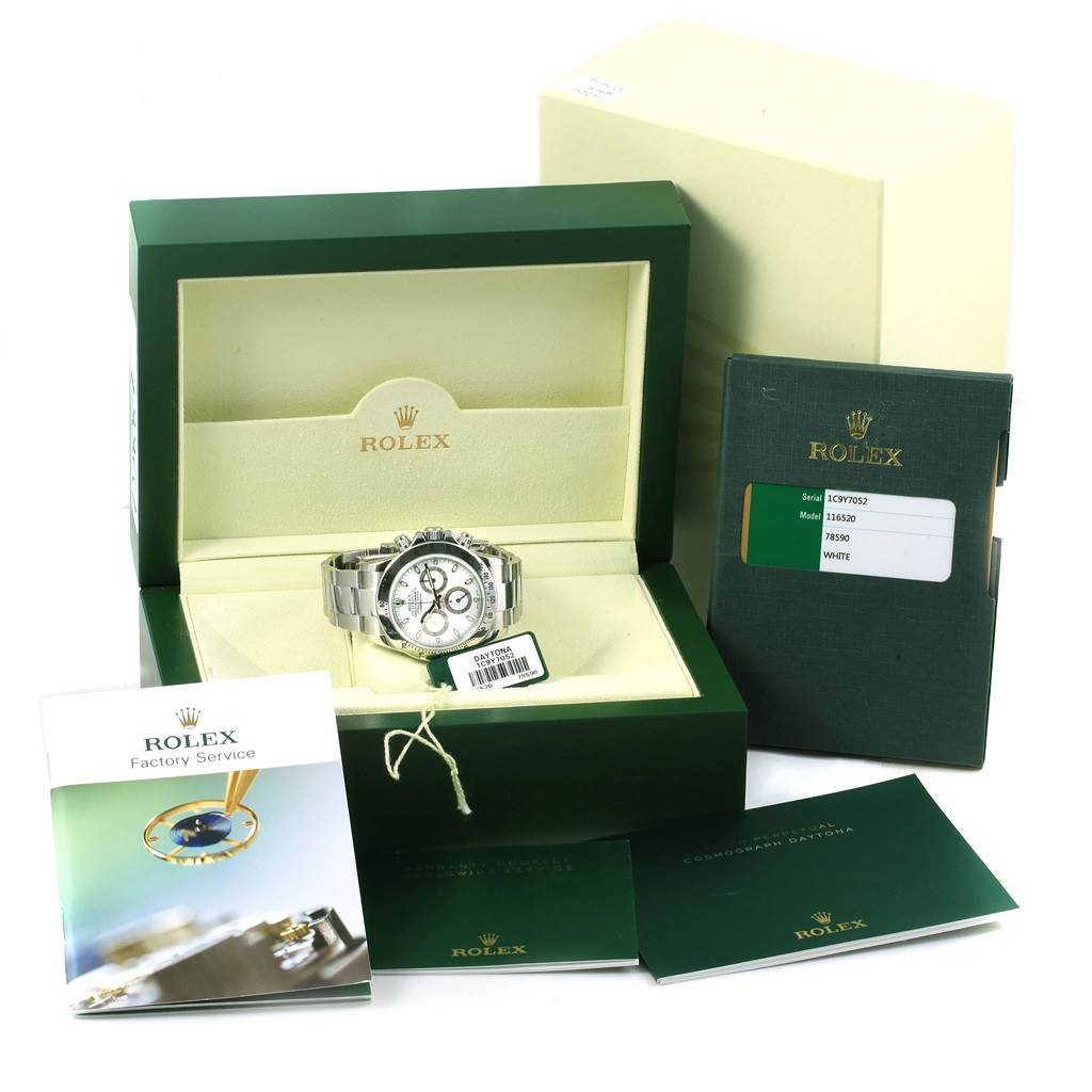 The image shows a Rolex Daytona 116520 Men
s Stainless Steel White Dial 116520 Men
s Stainless Steel White Dial watch angled from the front, within its box, surrounded by manuals and paperwork.