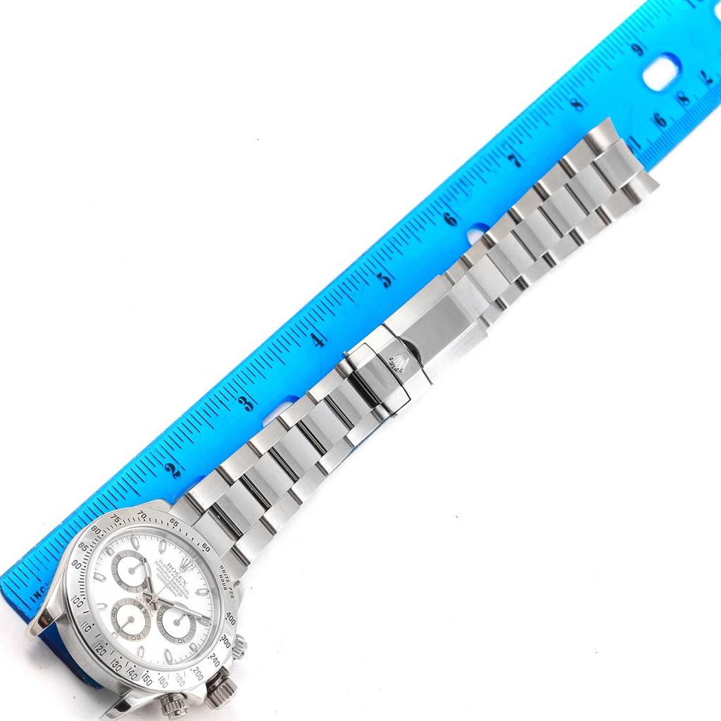 The image shows the front view of a Rolex Daytona 116520 Men
s Stainless Steel White Dial 116520 Men
s Stainless Steel White Dial watch, displaying the face, bezel, and bracelet next to a blue ruler.