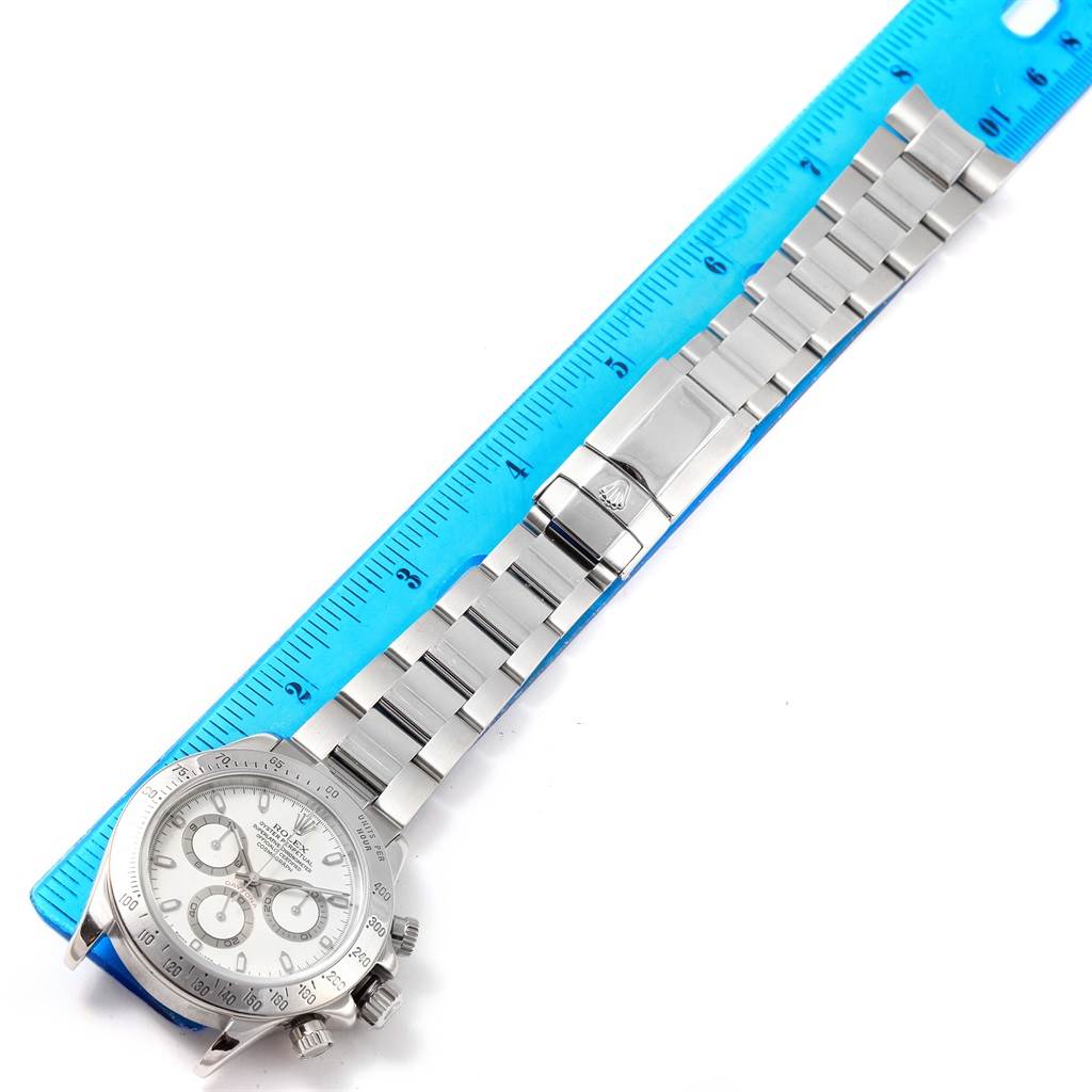 The image shows a top-down view of a Rolex Daytona 116520 Men's Stainless Steel White Dial 116520 Men's Stainless Steel White Dial watch with a focus on its face, bracelet, and clasp beside a ruler.