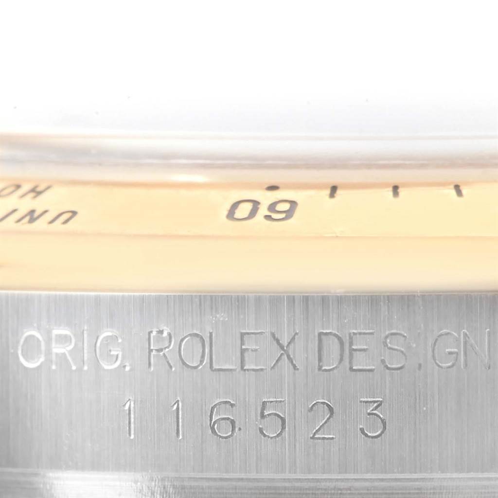 This image shows a close-up of the edge of the bezel and the engraved serial number on the side of a Rolex Daytona 116523 Men's Steel and Gold (two tone) Black Dial 116523 Men's Steel and Gold (two tone) Black Dial watch.
