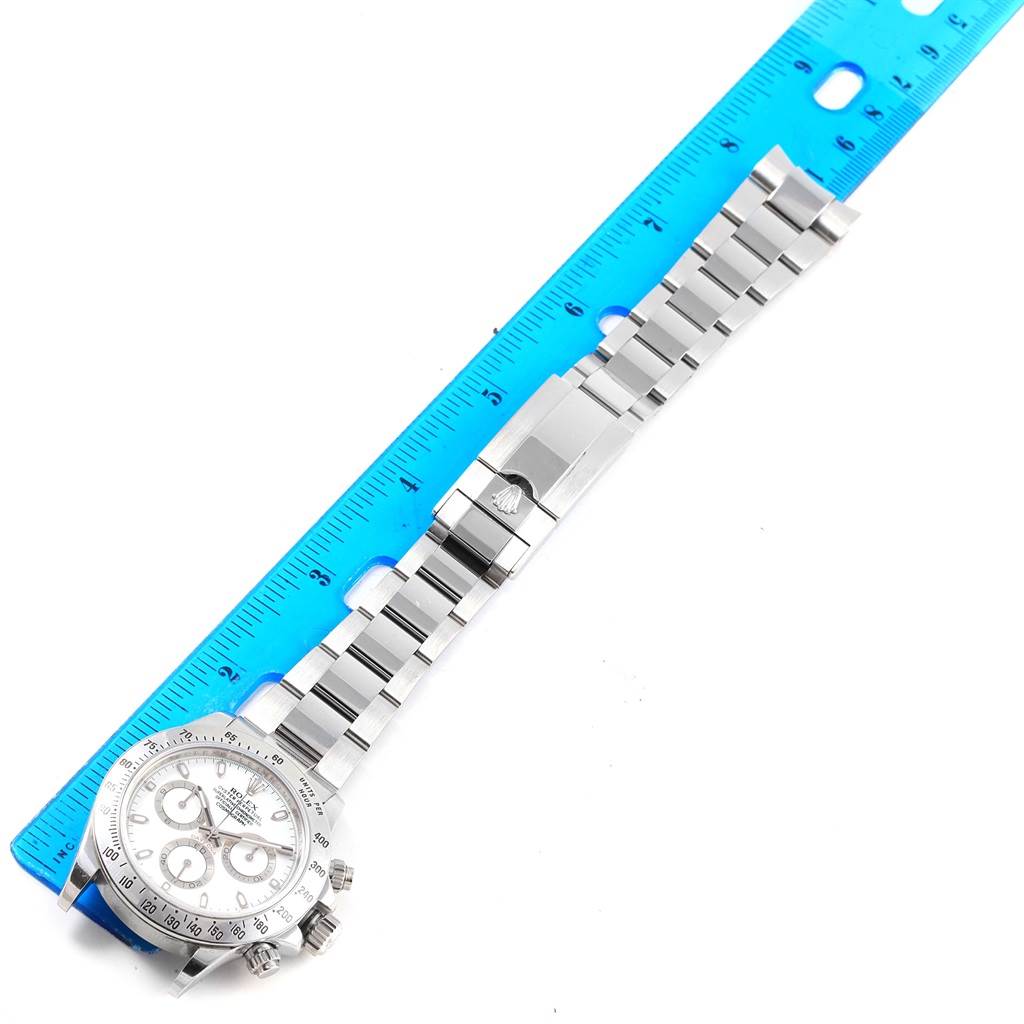 The image shows a Rolex Daytona 116520 Men's Stainless Steel White Dial 116520 Men's Stainless Steel White Dial watch laid flat next to a blue ruler, displaying the face, bezel, bracelet, and clasp.