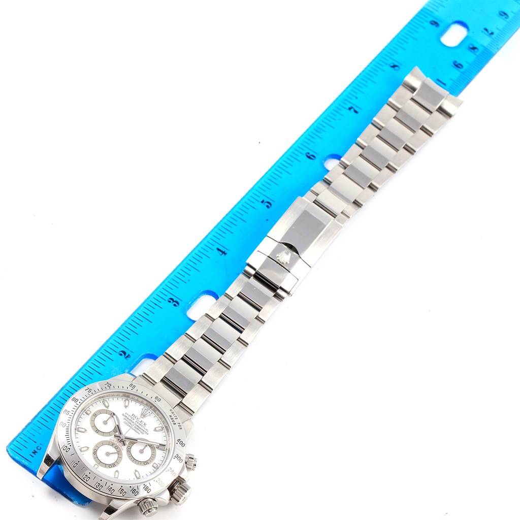 The Rolex Daytona 116520 Men's Stainless Steel White Dial 116520 Men's Stainless Steel White Dial watch is shown from an overhead angle, highlighting its face, bracelet, and clasp next to a blue ruler for scale.