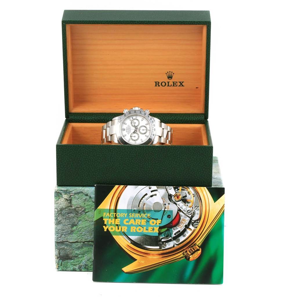 The image shows a front view of a Rolex Daytona 116520 Men's Stainless Steel White Dial 116520 Men's Stainless Steel White Dial watch in an open green box with a care booklet in front of the box.