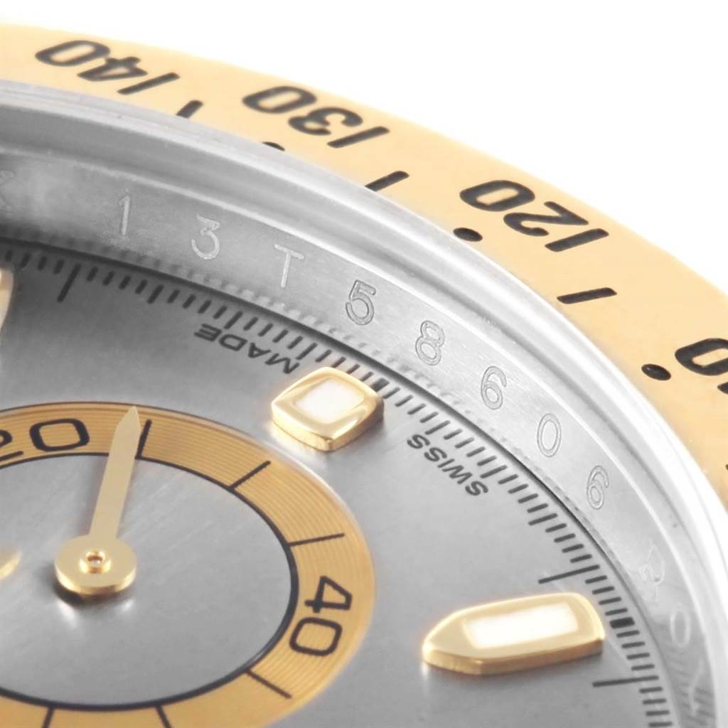 This close-up shot of the Rolex Daytona 116523 Men's Steel and Gold (two tone) Grey Dial 116523 Men's Steel and Gold (two tone) Grey Dial watch showcases the bezel, part of the dial, and hour markers.