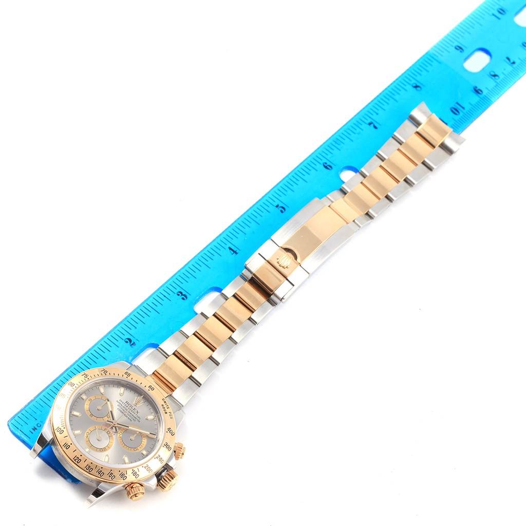 The Rolex Daytona 116523 Men's Steel and Gold (two tone) Grey Dial 116523 Men's Steel and Gold (two tone) Grey Dial watch is shown from a top view, displaying its dial, bezel, and bracelet alongside a ruler.