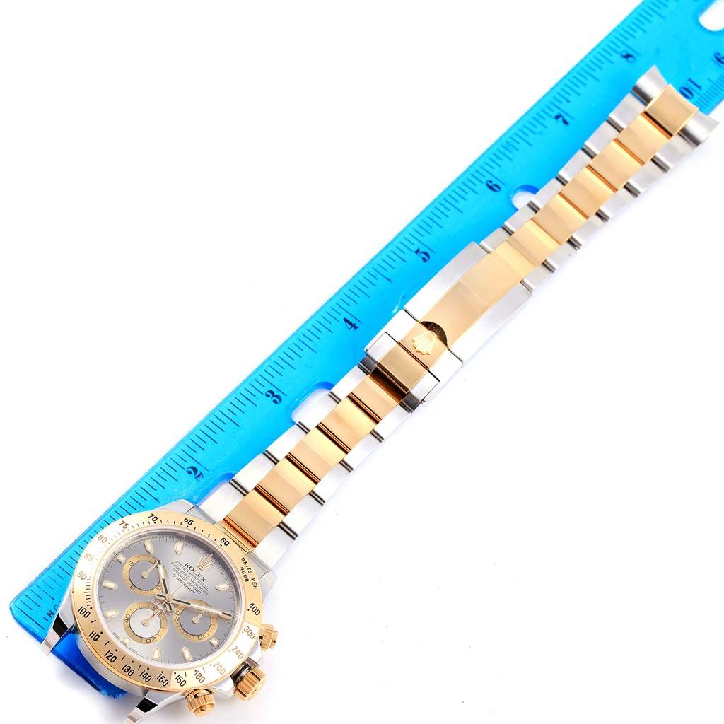 This image shows the front view of a Rolex Daytona 116523 Men's Steel and Gold (two tone) Grey Dial 116523 Men's Steel and Gold (two tone) Grey Dial watch alongside a blue ruler for measurement.