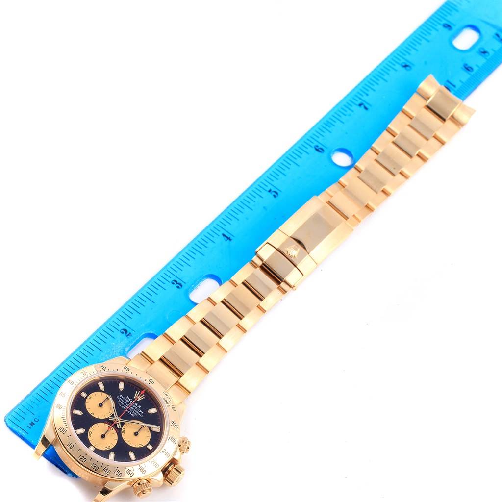 The image shows a full Rolex Daytona 116528 Men's Yellow Gold Black Dial 116528 Men's Yellow Gold Black Dial watch lying flat with a blue ruler beside it, highlighting the dial and bracelet.