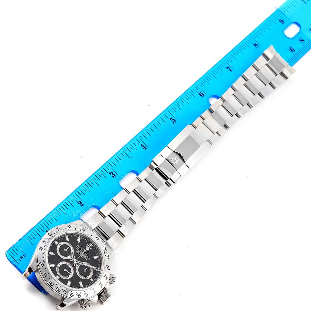 The image shows the face and band of a Rolex Daytona 116520 Men's Stainless Steel Black Dial 116520 Men's Stainless Steel Black Dial watch, alongside a blue ruler.