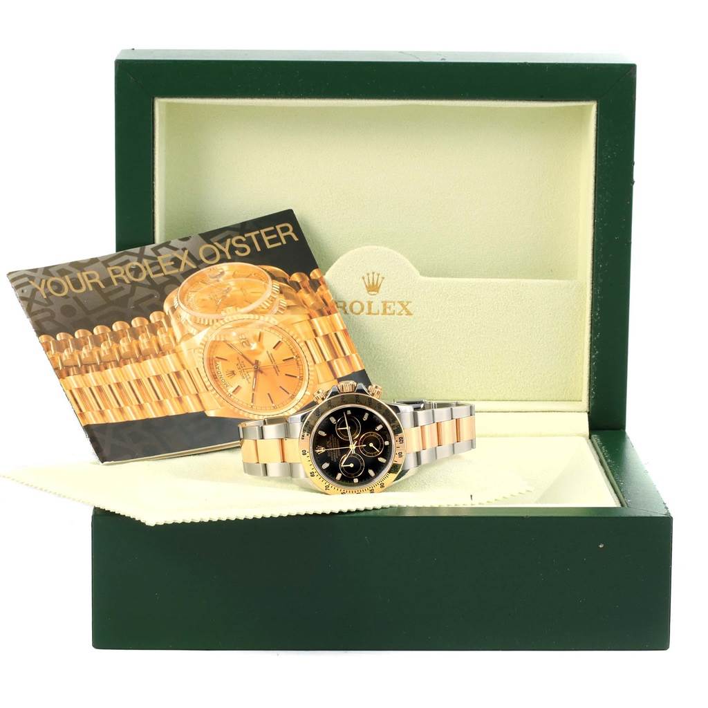 The image shows a Rolex Daytona 116523 Men's Steel and Gold (two tone) Black Dial 116523 Men's Steel and Gold (two tone) Black Dial watch with its booklet and box, displayed from a front angle.
