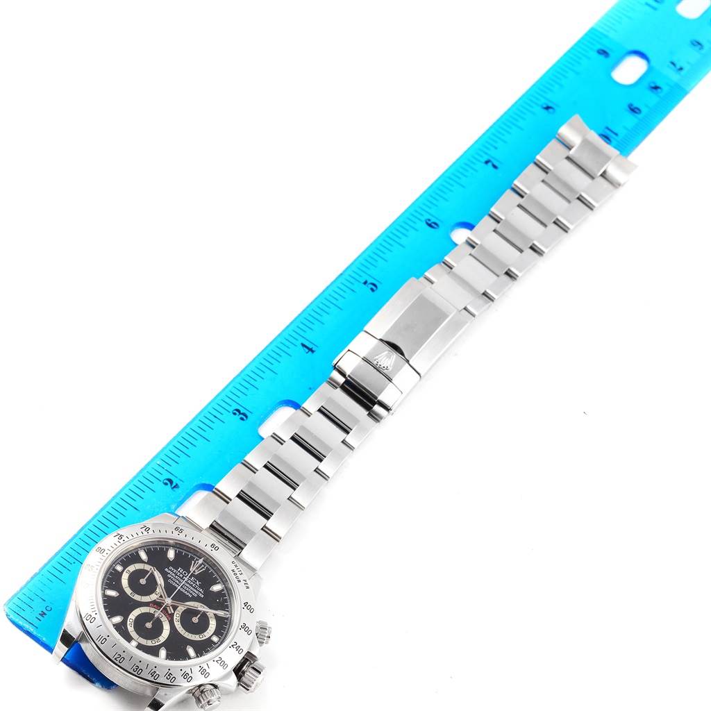 The image shows a top-down view of a Rolex Daytona 116520 Men's Stainless Steel Black Dial 116520 Men's Stainless Steel Black Dial watch, displaying the face, bezel, and metal bracelet against a ruler for scale.