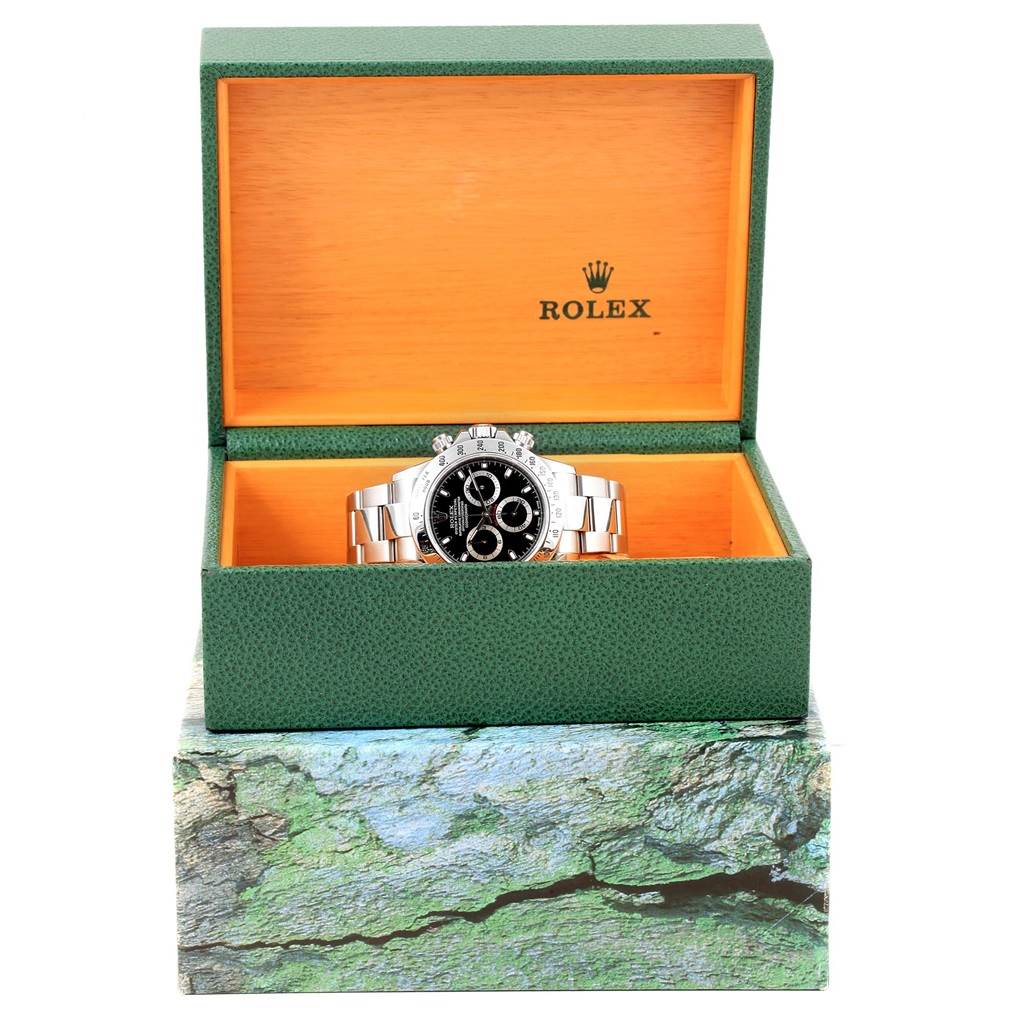 The image displays a Rolex Daytona 116520 Men's Stainless Steel Black Dial 116520 Men's Stainless Steel Black Dial watch front view inside its open green and orange presentation box.