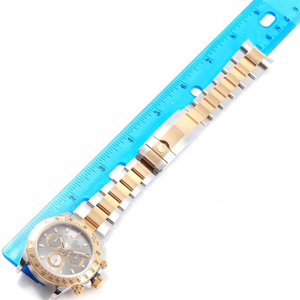 The Rolex Daytona 116523 Men's Stainless Steel Grey Dial 116523 Men's Stainless Steel Grey Dial watch is displayed flat on its side with a partial view of the face and the entire bracelet next to a ruler.