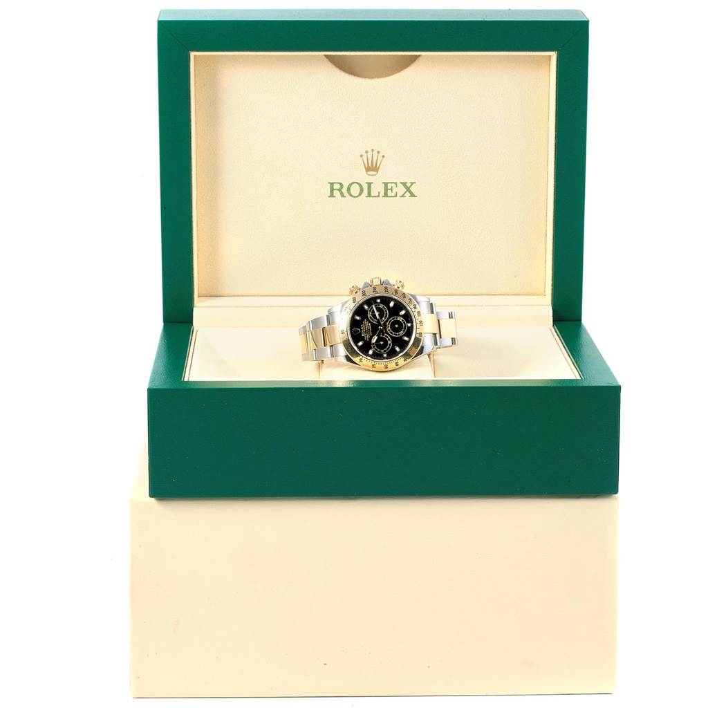 The Rolex Daytona 116523 Men's Steel and Gold (two tone) Black Dial 116523 Men's Steel and Gold (two tone) Black Dial watch is shown front-facing, displayed inside its green and cream-colored branded box.