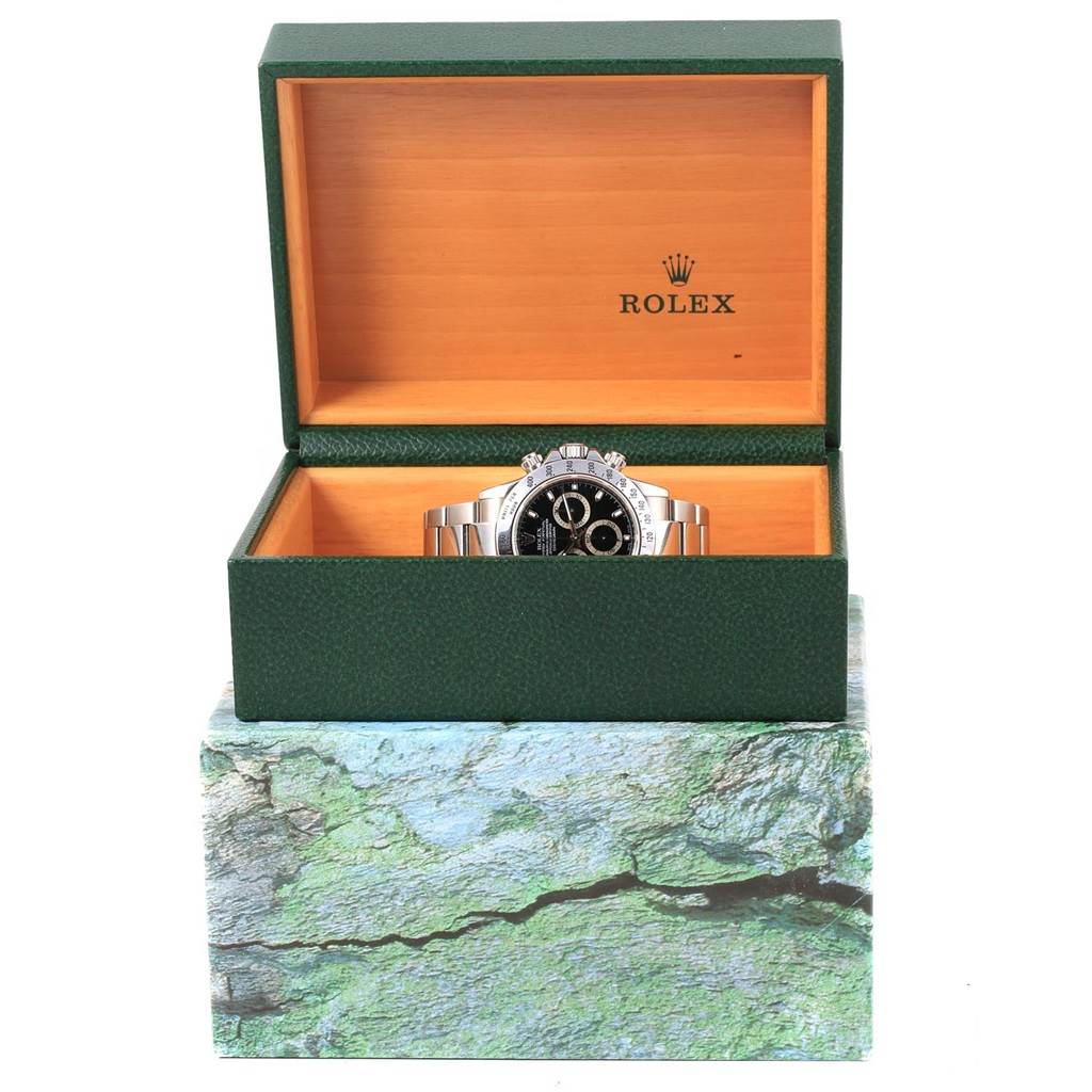 The Rolex Daytona 116520 Men's Stainless Steel Black Dial 116520 Men's Stainless Steel Black Dial watch is shown front-on inside its green and wooden box, revealing the dial and part of the bracelet.