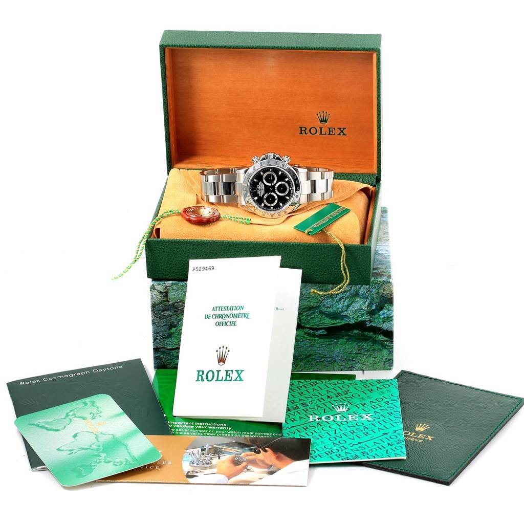 The Rolex Daytona 116520 Men's Stainless Steel Black Dial 116520 Men's Stainless Steel Black Dial watch is displayed head-on in its open box, with various informative booklets and a tag around it.