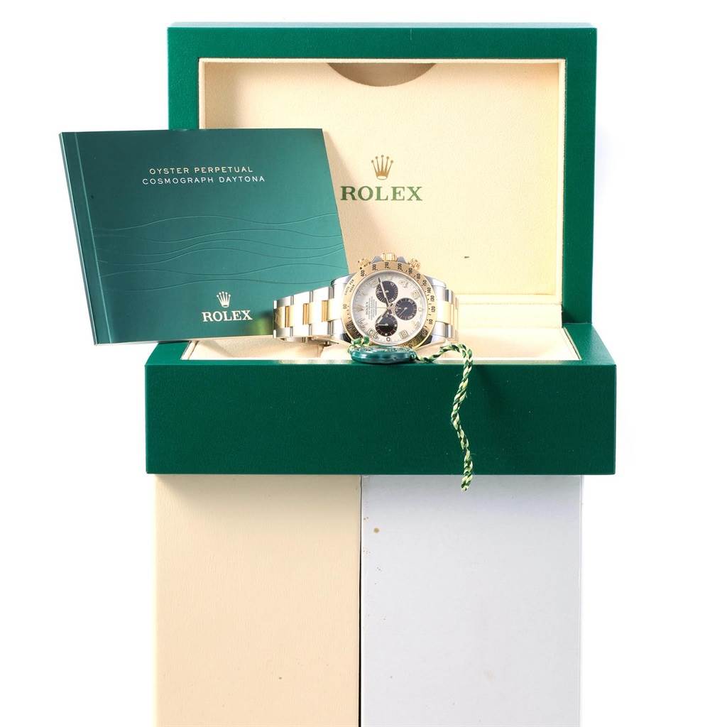 The image shows a Rolex Daytona 116523 Men's Steel and Gold (two tone) White Dial 116523 Men's Steel and Gold (two tone) White Dial watch front and center, placed inside its green box, with an instruction manual propped beside it.