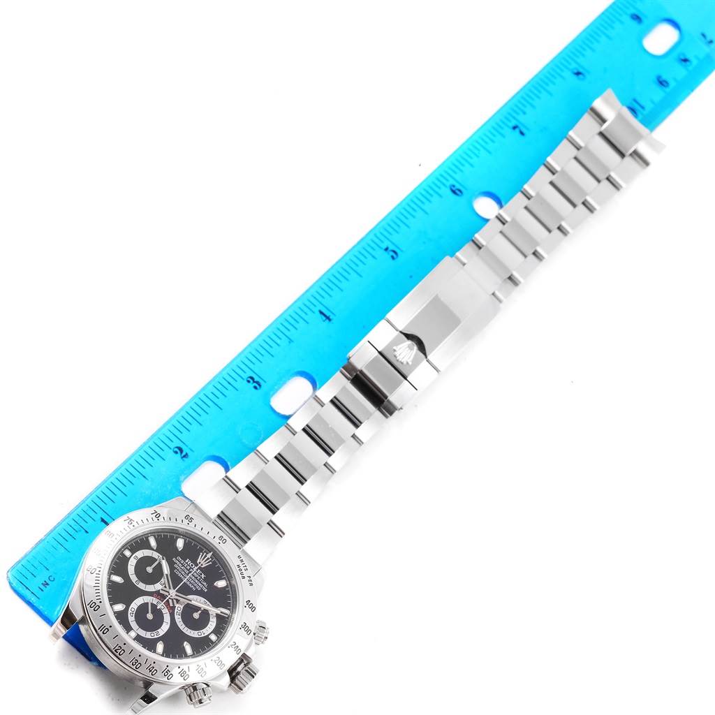 The image shows a Rolex Daytona 116520 Men's Stainless Steel Black Dial 116520 Men's Stainless Steel Black Dial watch laid flat with its face and metal bracelet band fully visible alongside a blue ruler.