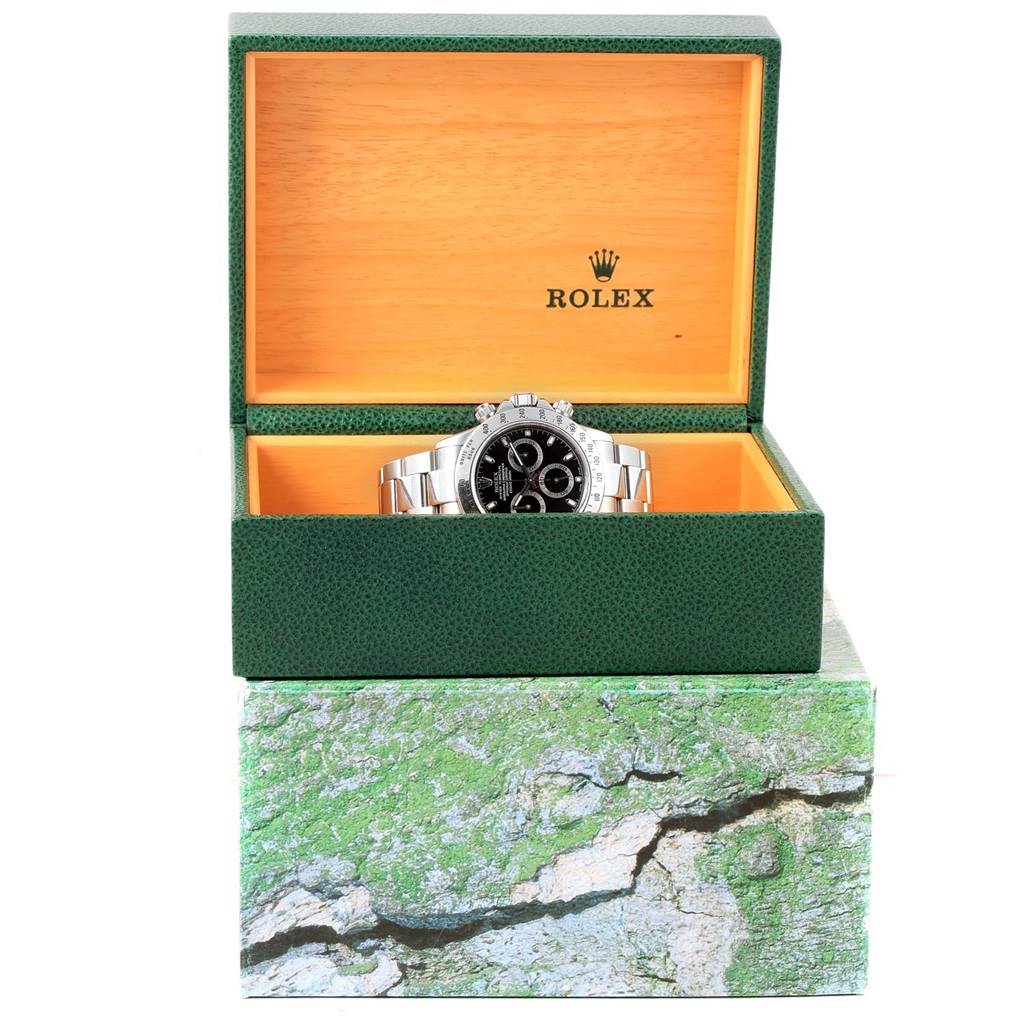 The Rolex Daytona 116520 Men's Stainless Steel Black Dial 116520 Men's Stainless Steel Black Dial watch is shown front-facing in an open green and yellow watch box with the Rolex logo visible inside.