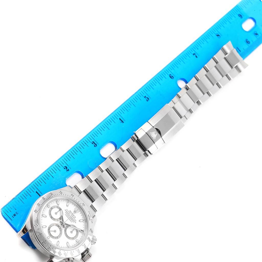 The image shows the Rolex Daytona 116520 Men's Stainless Steel White Dial 116520 Men's Stainless Steel White Dial watch lying flat with its bracelet extended alongside a blue ruler for scale.