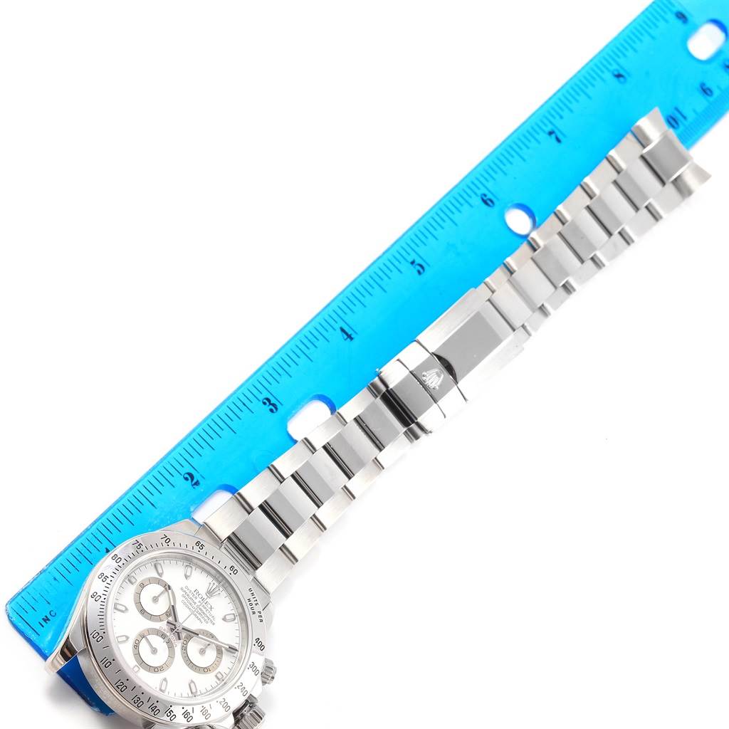 The image shows a top-down view of a Rolex Daytona 116520 Men's Stainless Steel White Dial 116520 Men's Stainless Steel White Dial watch with its bracelet next to a blue ruler for measurement.