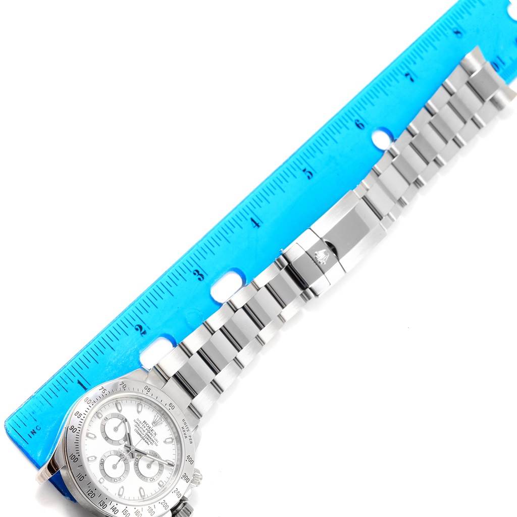 The image shows a Rolex Daytona 116520 Men's Stainless Steel White Dial 116520 Men's Stainless Steel White Dial watch placed next to a blue ruler, with a focus on the bracelet and clasp.