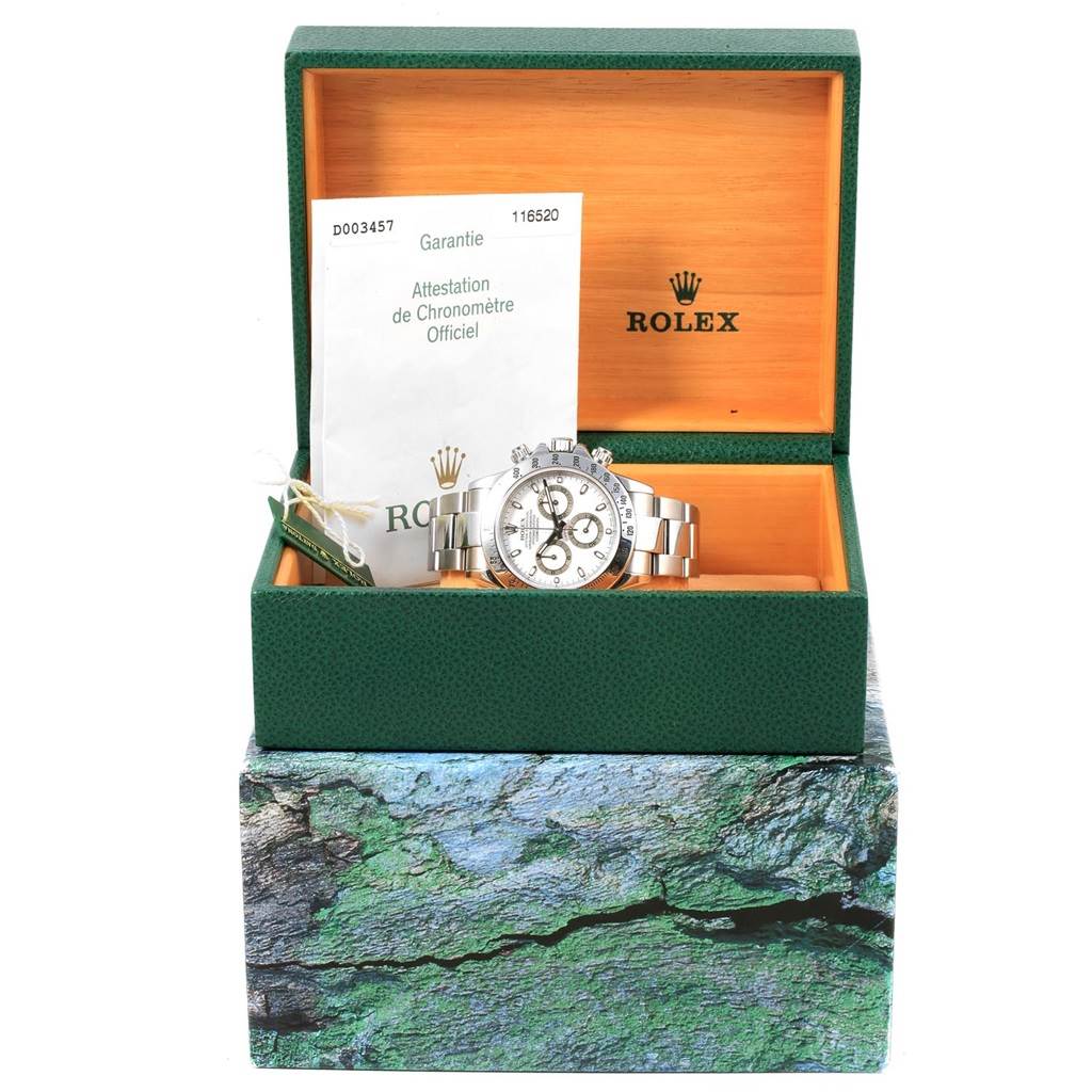 The image shows a Rolex Daytona 116520 Men
s Stainless Steel White Dial 116520 Men
s Stainless Steel White Dial watch placed in an open green Rolex box with its warranty paper inside.