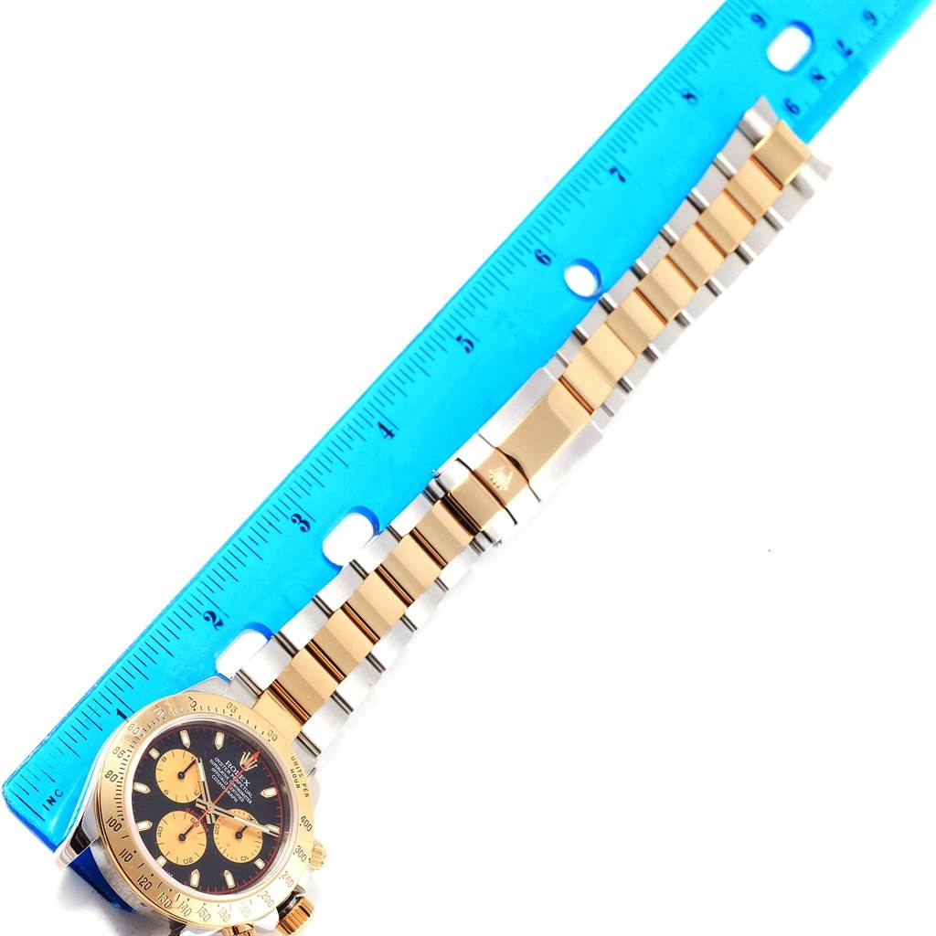 The image shows the Rolex Daytona 116523 Men's Steel and Gold (two tone) Black Dial 116523 Men's Steel and Gold (two tone) Black Dial watch from an overhead angle, highlighting the band and partial face, with a ruler for scale.