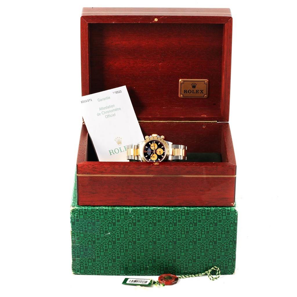 The watch is a Rolex Daytona 116523 Men's Steel and Gold (two tone) Black Dial 116523 Men's Steel and Gold (two tone) Black Dial, displayed inside its open wooden box with accompanying paperwork and a green exterior box.