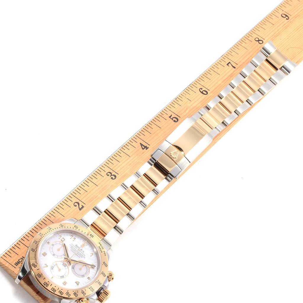 The Rolex Daytona 116523 Men's Steel and Gold (two tone) Mother of Pearl Dial 116523 Men's Steel and Gold (two tone) Mother of Pearl Dial watch is shown with its face and bracelet parallel to a ruler, highlighting the length and design details.