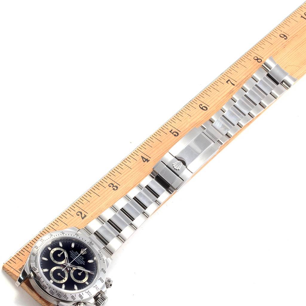 The image shows a Rolex Daytona 116520 Men's Stainless Steel Black Dial 116520 Men's Stainless Steel Black Dial watch laid flat with its bracelet extended alongside a wooden ruler for measurement.