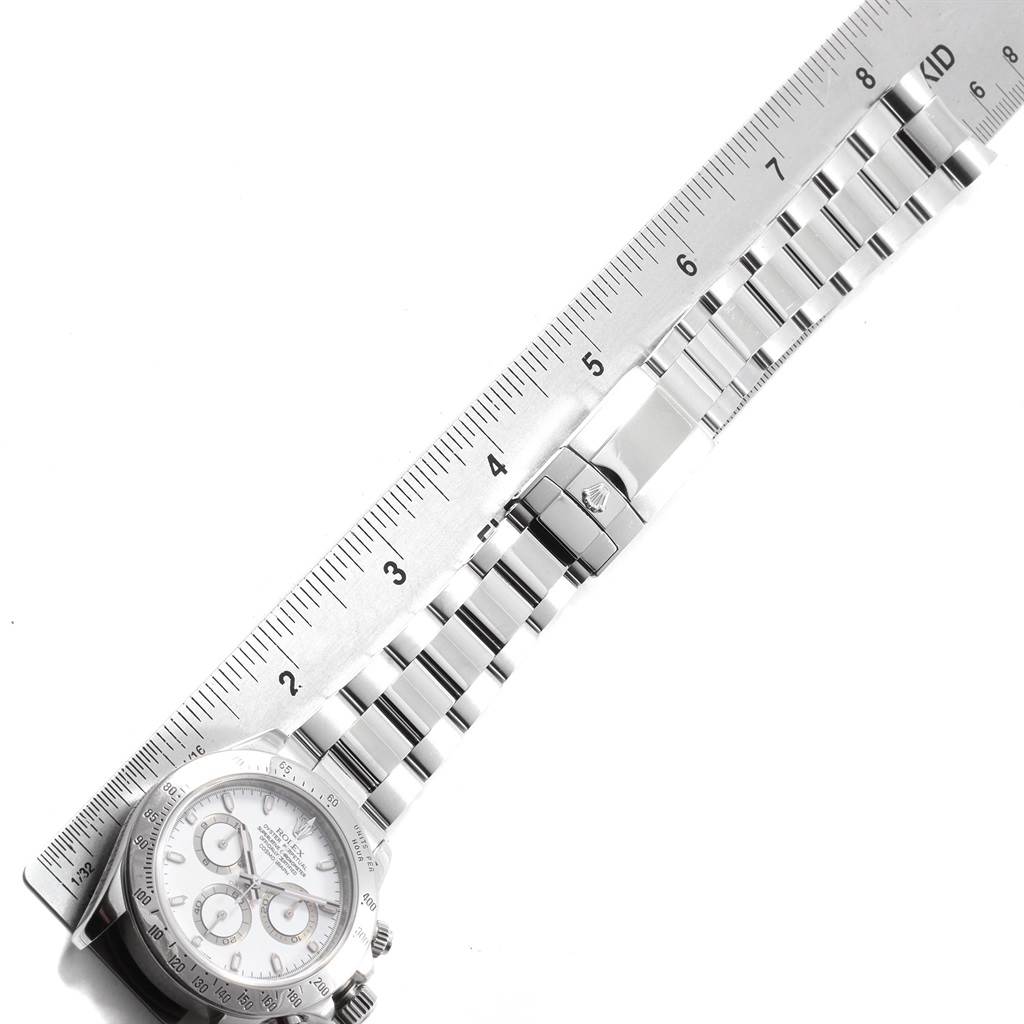 This image shows the face and bracelet of a Rolex Daytona 116520 Men's Stainless Steel White Dial 116520 Men's Stainless Steel White Dial watch placed alongside a ruler.