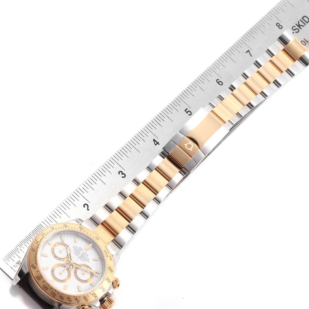 The image shows a Rolex Daytona 116523 Men's Steel and Gold (two tone) White Dial 116523 Men's Steel and Gold (two tone) White Dial watch positioned alongside a ruler, displaying the face and part of the bracelet.