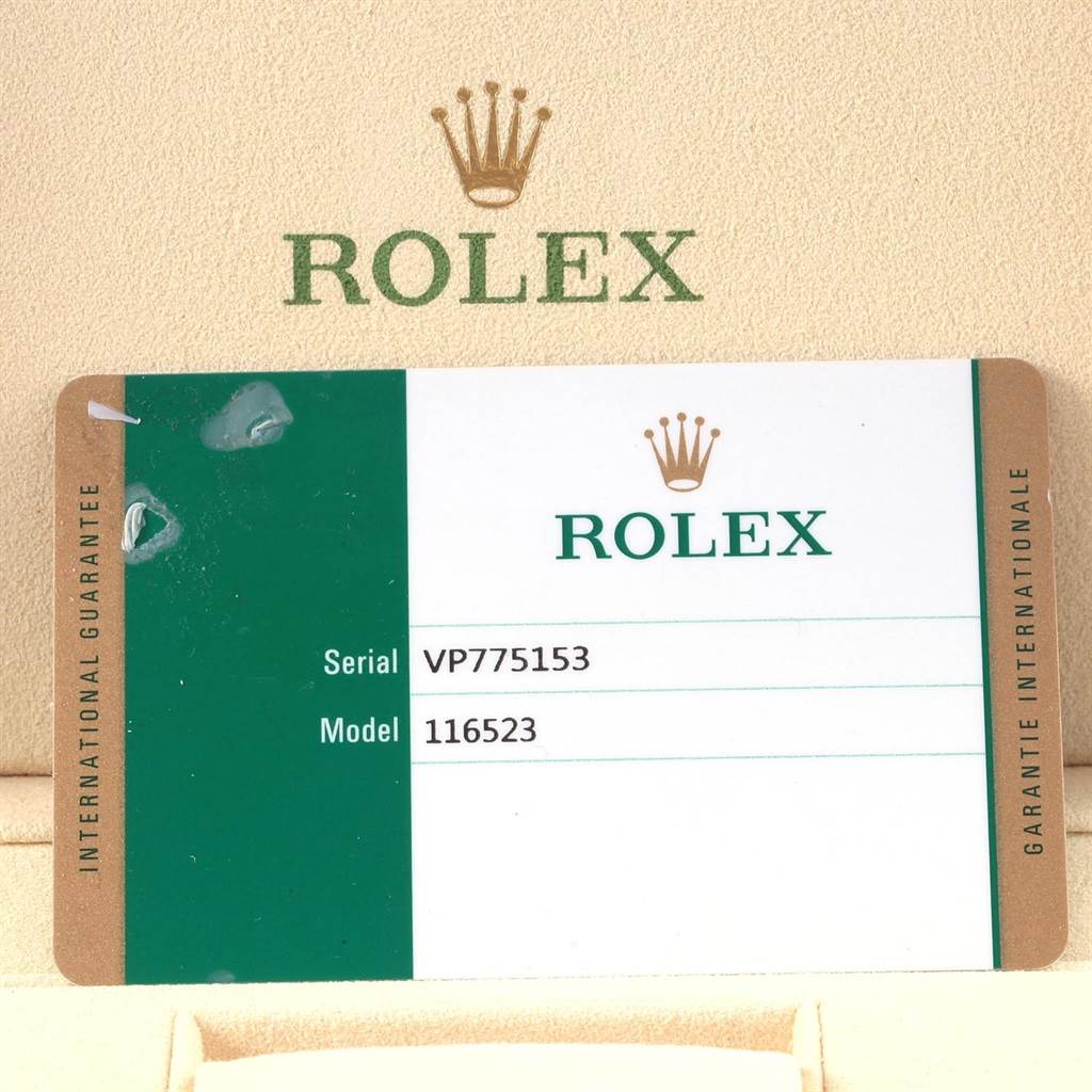 The image shows an international guarantee card and box for a Rolex Daytona 116523 Men's Steel and Gold (two tone) White Dial 116523 Men's Steel and Gold (two tone) White Dial model, with prominent branding and serial/model details.