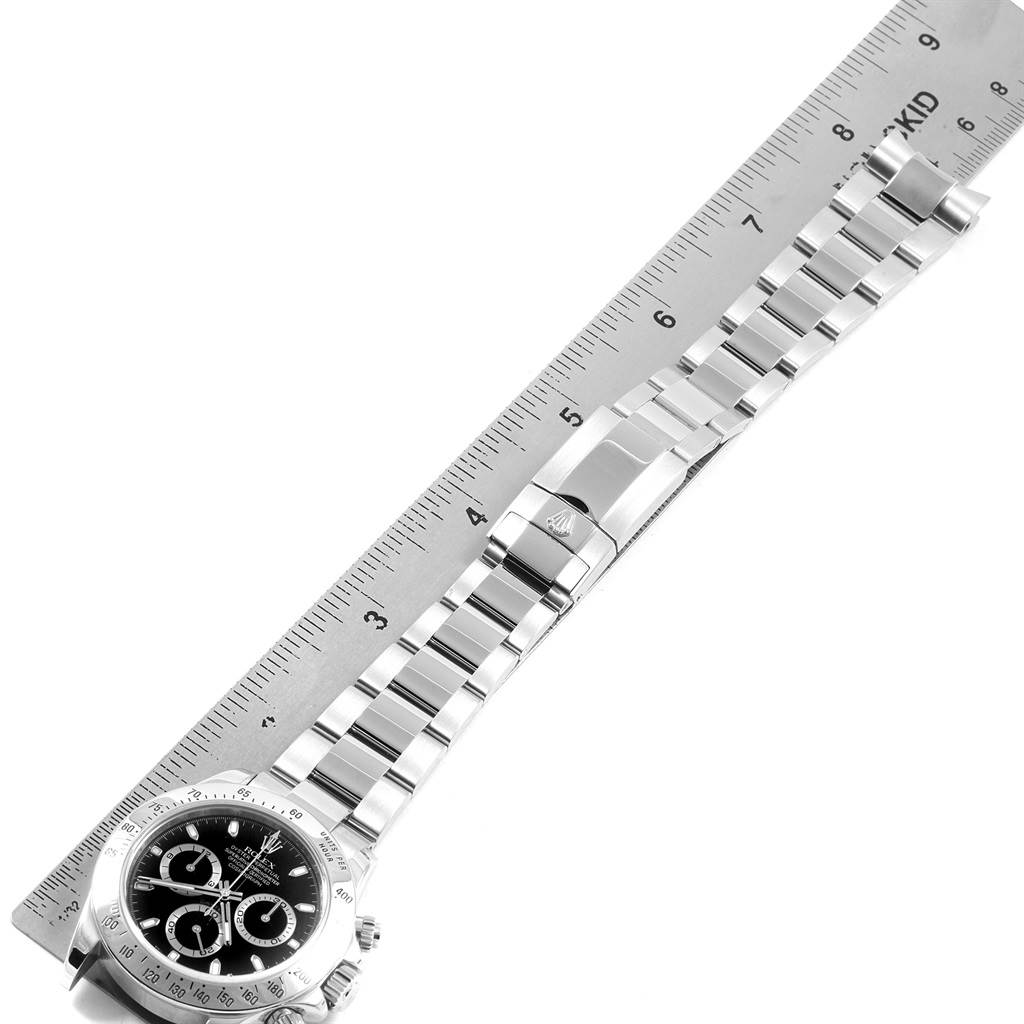 The image shows a top-down view of the bezel, dial, bracelet, and clasp of a Rolex Daytona 116520 Men's Stainless Steel Black Dial 116520 Men's Stainless Steel Black Dial watch next to a ruler.