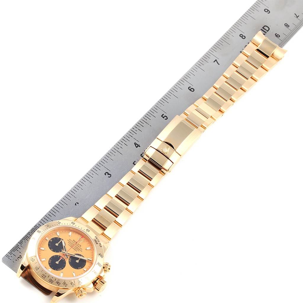 The Rolex Daytona 116528 Men's Yellow Gold Champagne Dial 116528 Men's Yellow Gold Champagne Dial watch is shown from a top angle, displaying the face, bracelet, and clasp alongside a ruler for scale.