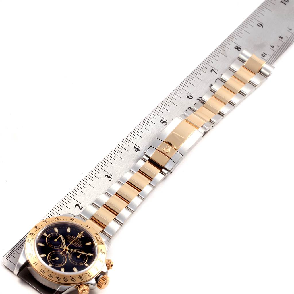 This image shows the Rolex Daytona 116523 Men's Steel and Gold (two tone) Black Dial 116523 Men's Steel and Gold (two tone) Black Dial watch placed next to a ruler, highlighting the dial, bezel, and part of the bracelet.