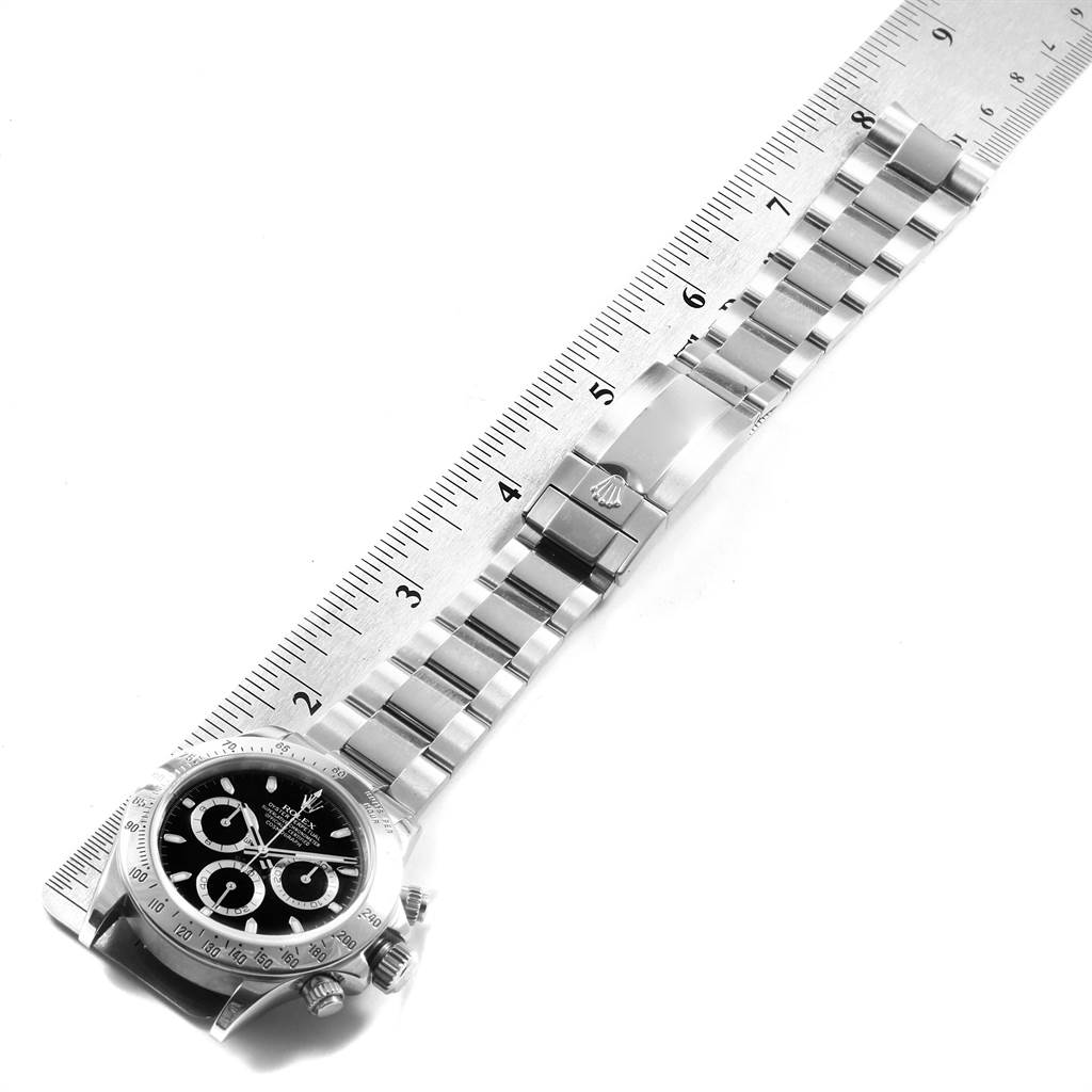 The image shows an overhead view of a Rolex Daytona 116520 Men
s Stainless Steel Black Dial 116520 Men
s Stainless Steel Black Dial watch with its metal bracelet aligned next to a ruler for measurement.
