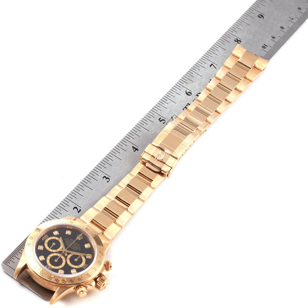 This image shows a gold Rolex Daytona 16528 Men's Yellow Gold Black Dial 16528 Men's Yellow Gold Black Dial watch at a slight side angle with the entire bracelet and clasp visible, next to a ruler.